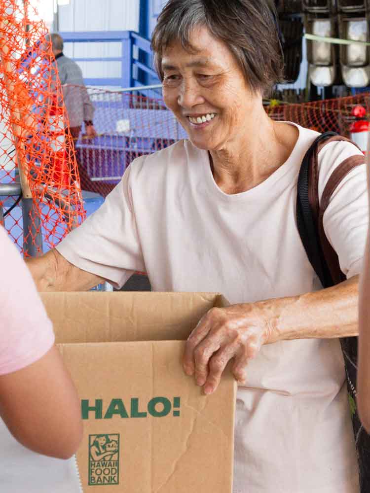 Smiling elderly woman receiving a Senior Food Box filled with nutritious food from Hawaii Foodbank, ensuring food security for kupuna.