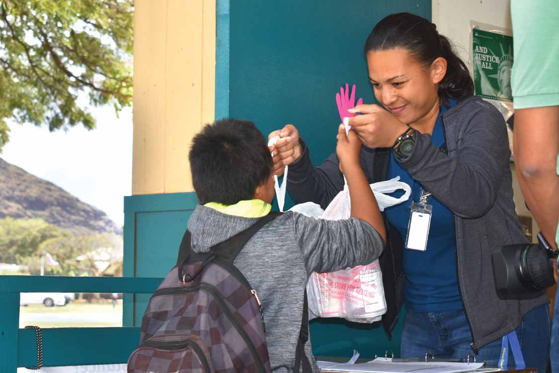 Volunteer distributing school pantry supplies to a young participant in the Food for Keiki program in Hawaii.